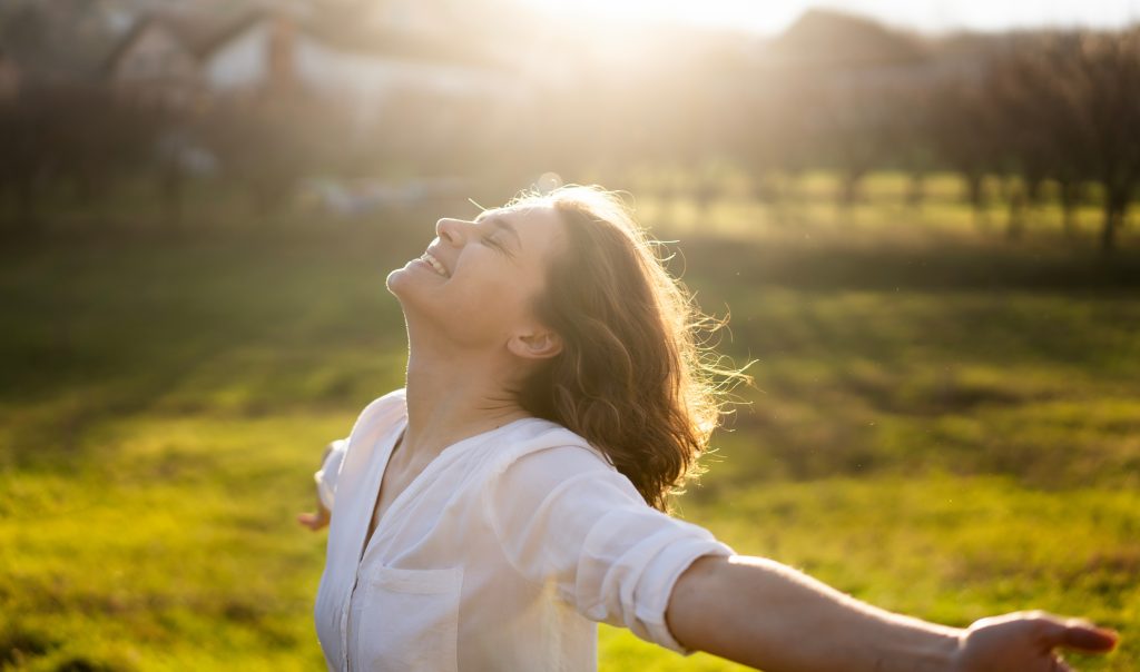 Young caucasian woman enjoying the sun and summer in a green field in the rays of the sun